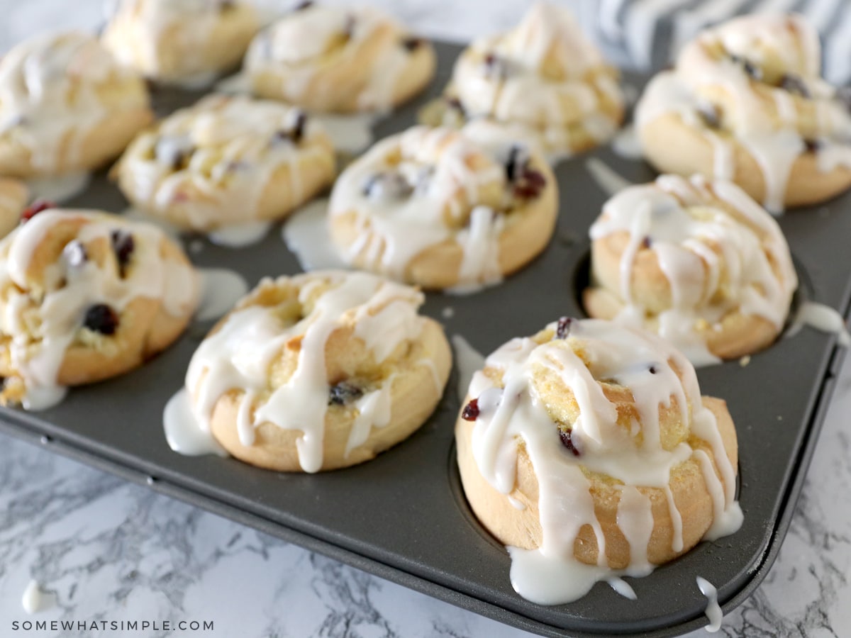 cranberry orange sweet rolls in a muffin tin drizzled with glaze