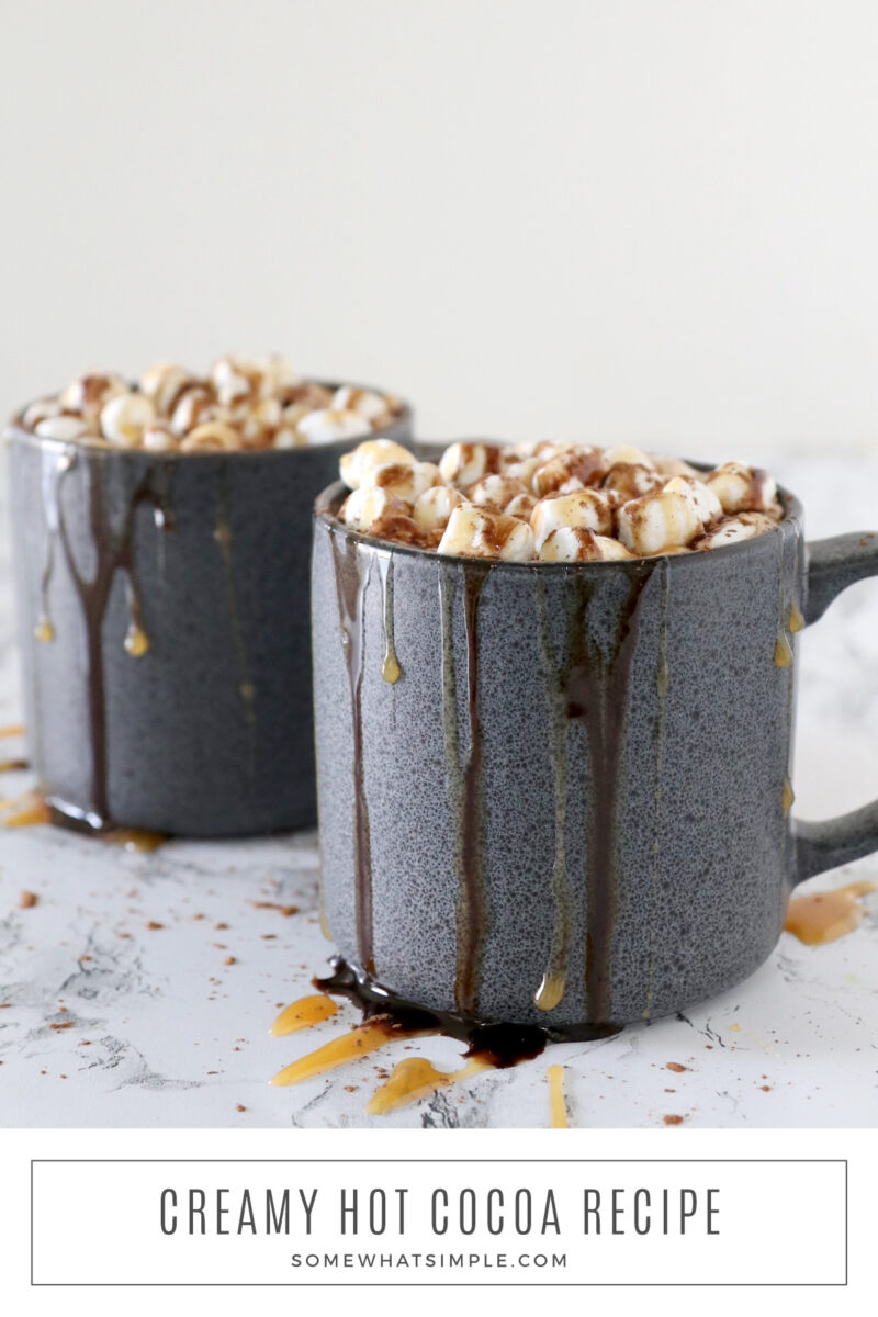 long image of creamy hot cocoa in 2 dark mugs