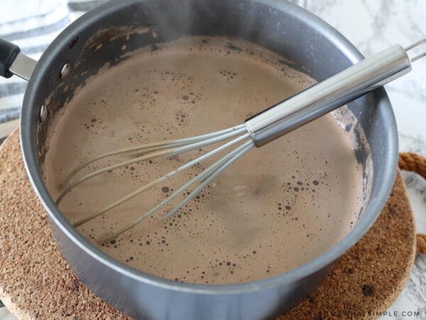adding milk to hot cocoa pot on stove