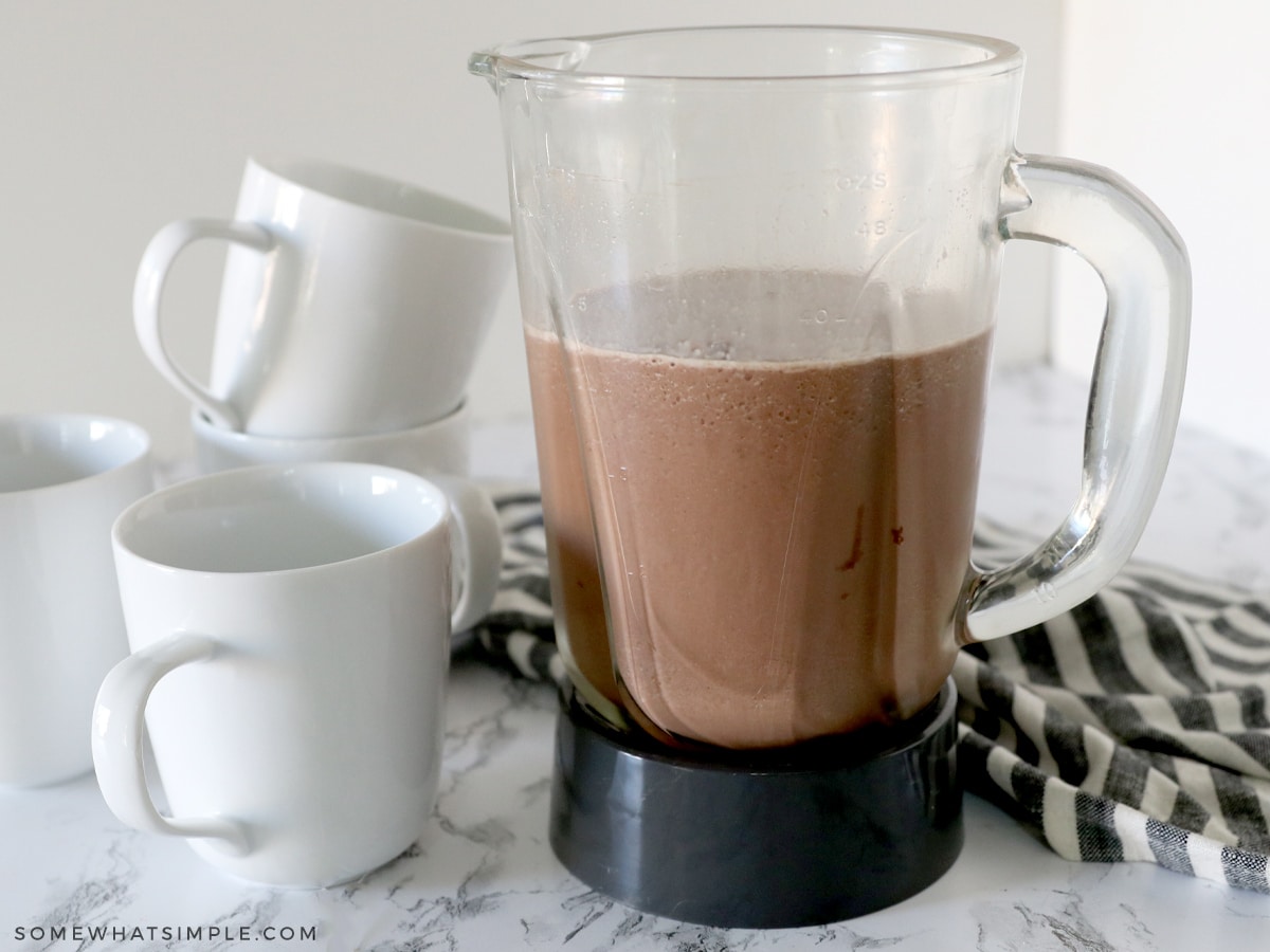 blender with hot chocolate next to some white mugs