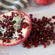 half of a pomegranate sliced open with a pile of seeds laying next to it