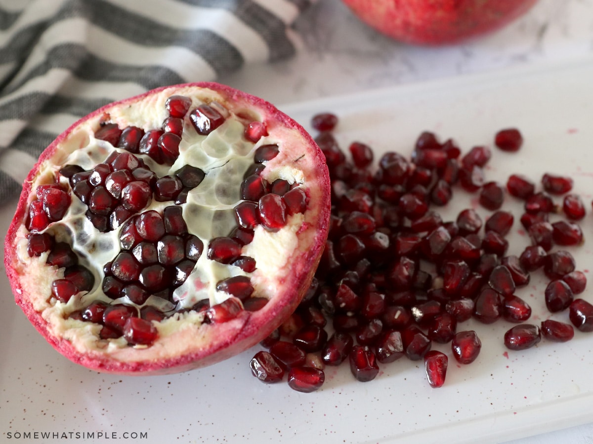 half of a pomegranate sliced open with a pile of seeds laying next to it