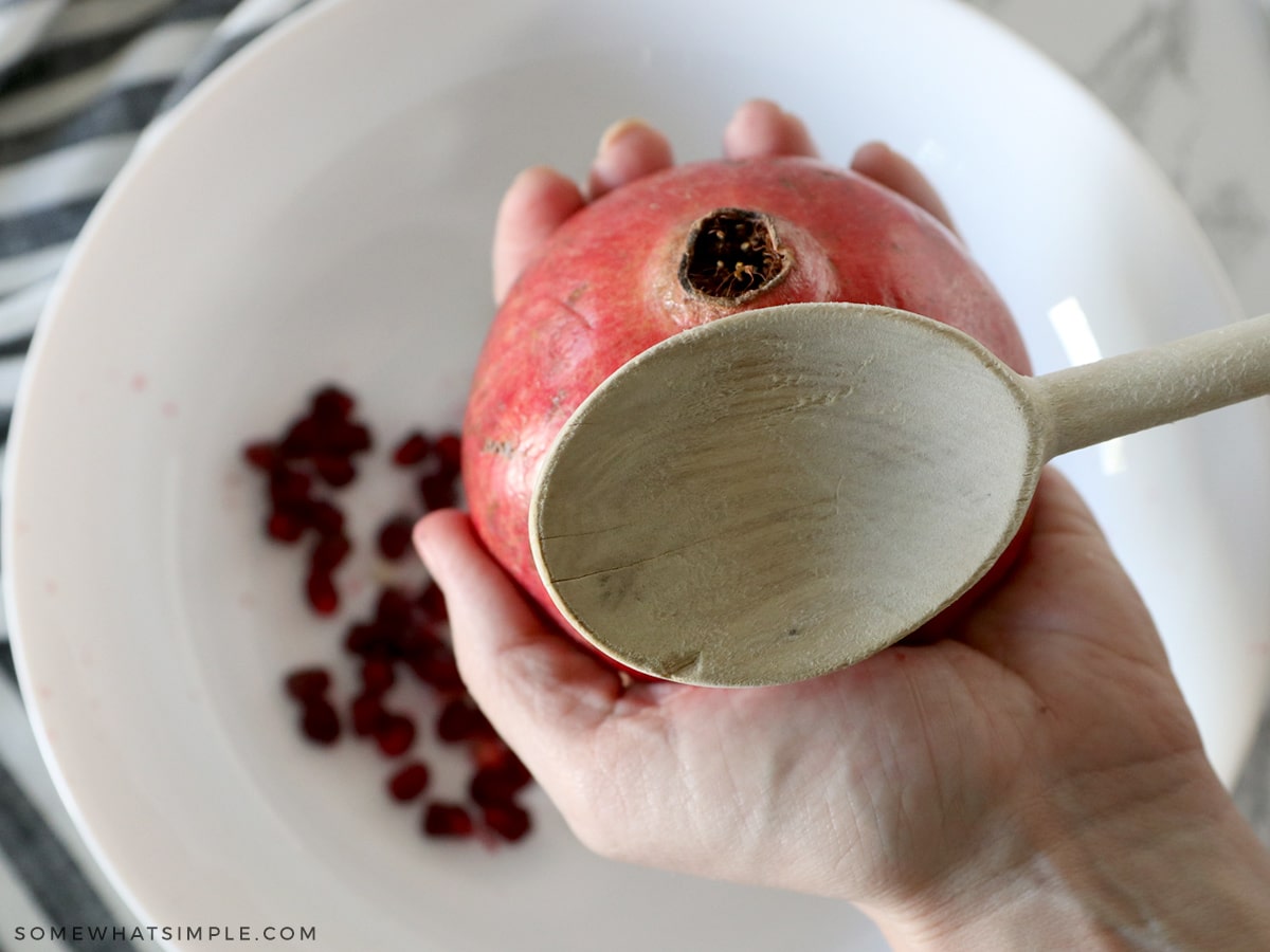 smacking half a pomegranate with the back of a wooden spoon