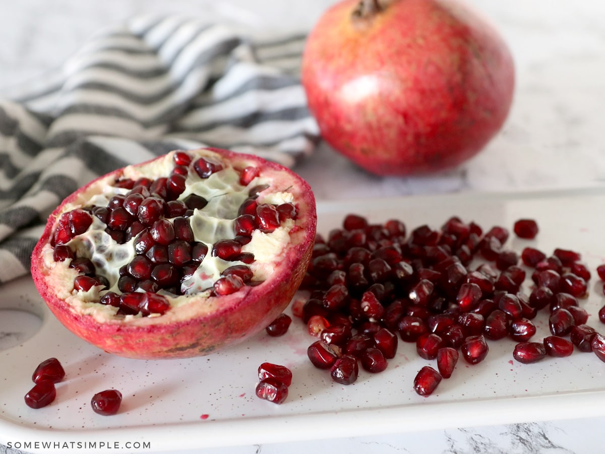 pomegranate seeds in a pile next to an intact half of a pomegranate 