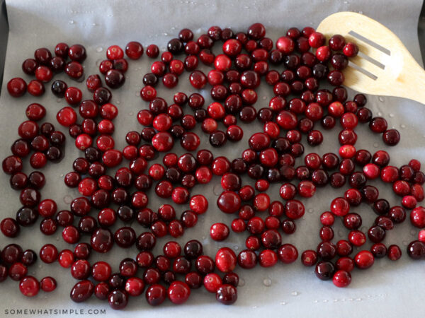 cranberries coated with a clear syrup laying on a piece of parchment paper
