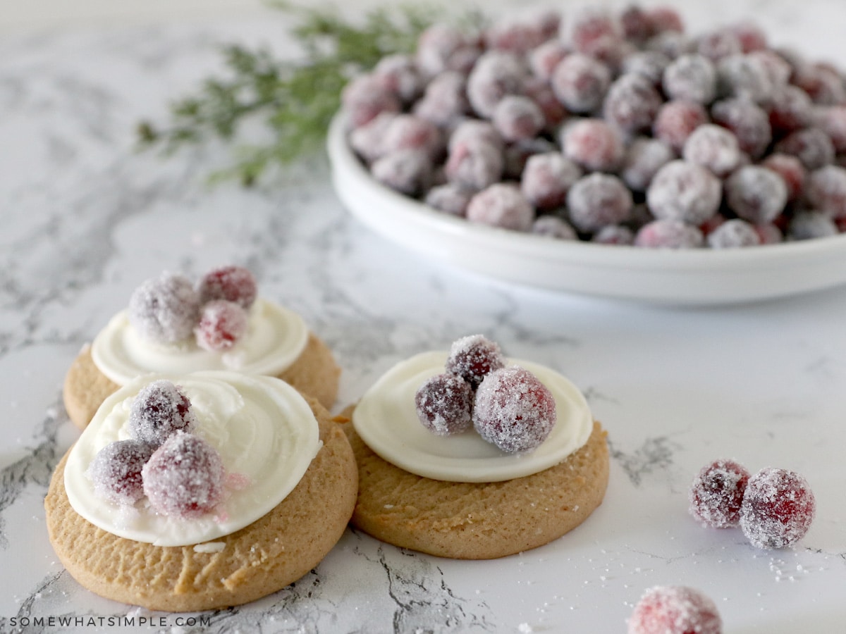 sugared cranberries on top of cookies with a plate of more cranberries in the background