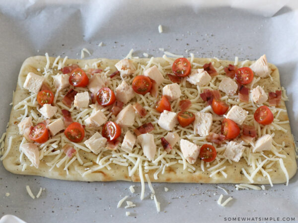 adding diced chicken and tomatoes to california chicken flatbread