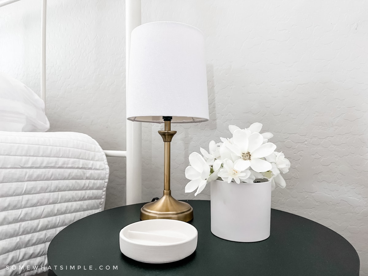 black round nightstand with a gold lamp and pot of flowers