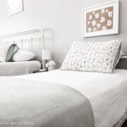 close up of a twin bed with a white quilt and green blanket at the foot