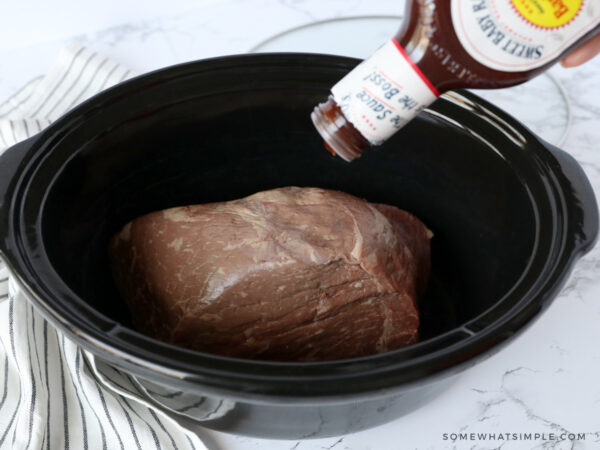 pouring BBQ sauce on top of a roast in a crockpot