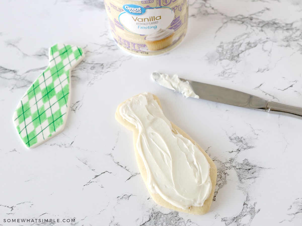 adding white frosting to a sugar cookie in the shape of a tie