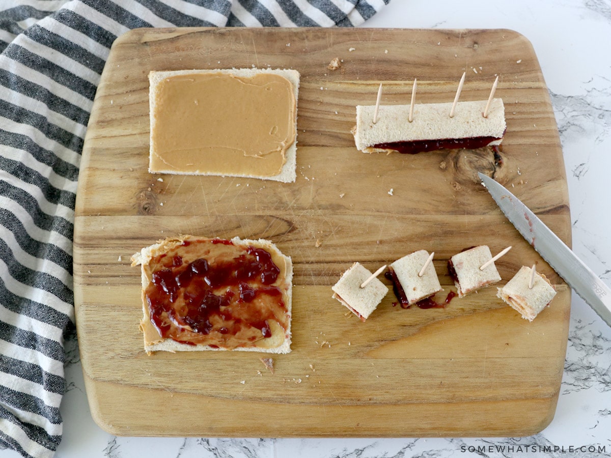 spreding peanut butter and jelly on sandwich bread, then cutting them and rolling them up into small pinwheels