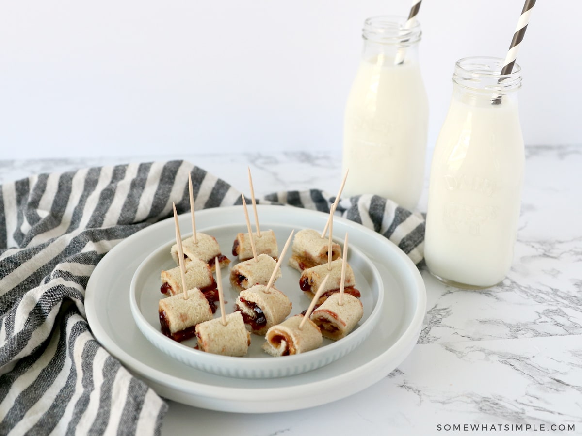 pinwheel sandwiches on a white plate next to a cup of milk