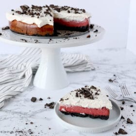 a slice of red velvet oreo cheesecake in the foreground and the whole cake in the background
