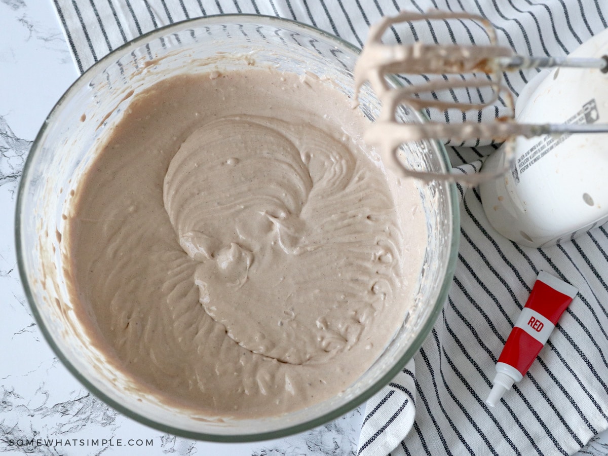 adding red food coloring to a bowl of cheesecake mixture