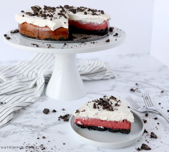 a slice of red velvet oreo cheesecake in the foreground and the whole cake in the background
