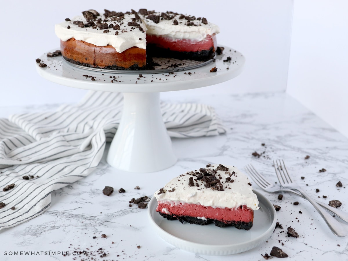 a slice of red velvet oreo cheesecake in the foreground and the whole cake in the background