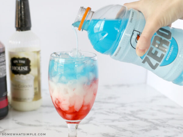 adding blue gatorade to a glass with red and white liquid