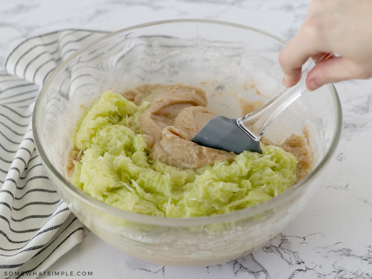 adding zucchini to a bowl of batter