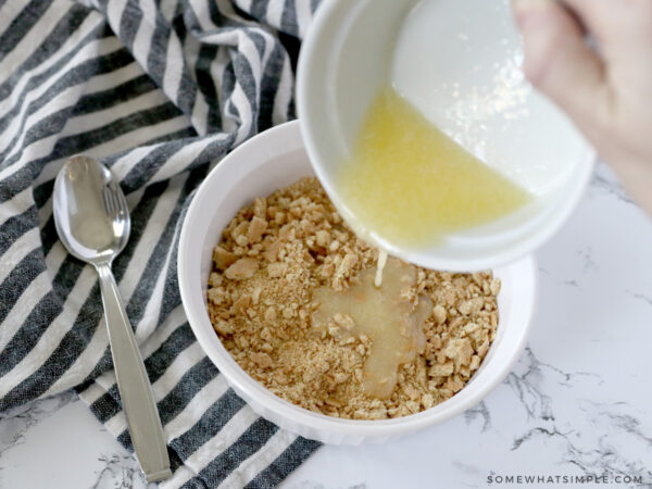 adding melted butter to a bowl of graham crackers