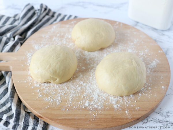 three balls of bread dough on a round cutting board