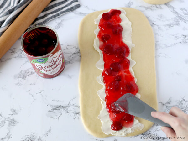 adding cream cheese and strawberry filling to raw bread dough