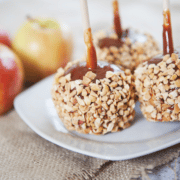 candy apples on a stick on a white plate next to a few fresh apples