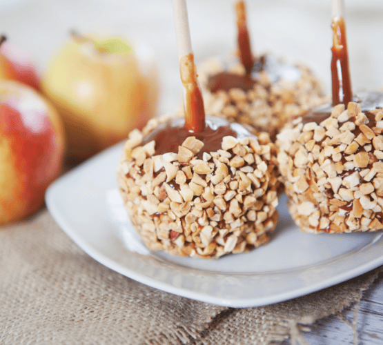 candy apples on a stick on a white plate next to a few fresh apples