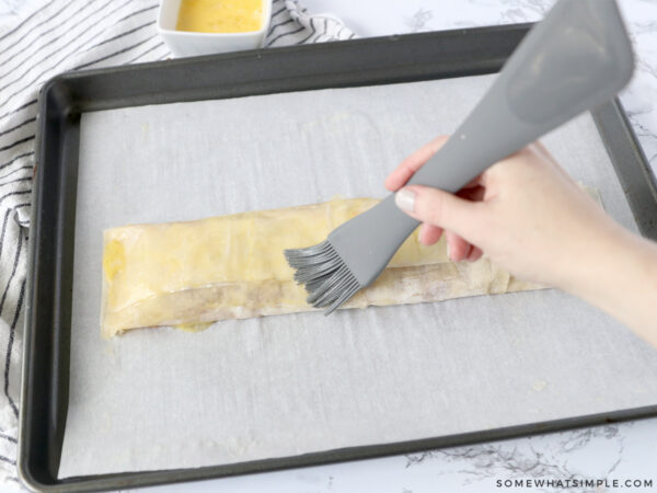 brushing filo dough rolled over cherry filling with melted butter