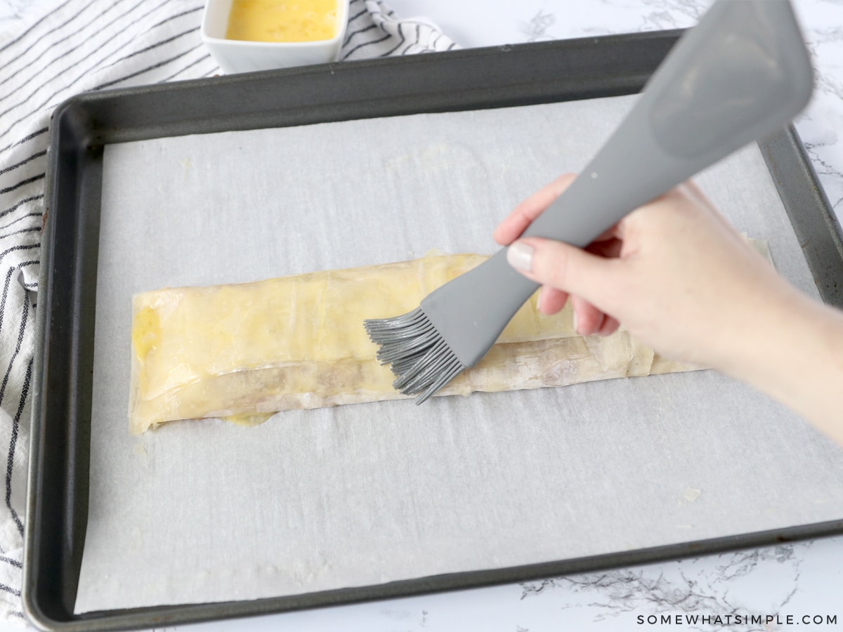 brushing filo dough rolled over cherry filling with melted butter