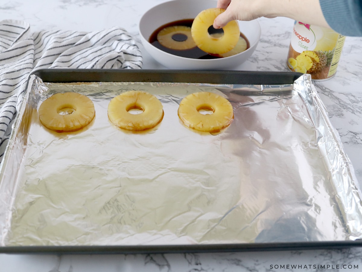 dipping pineapple into teriyaki sauce, then adding them to a baking sheet