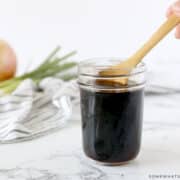 dipping a wooden spoon into a small jar of teriyaki sauce