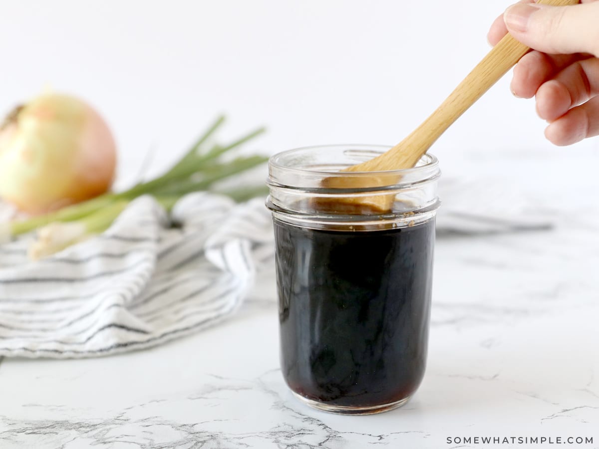 dipping a wooden spoon into a small jar of teriyaki sauce