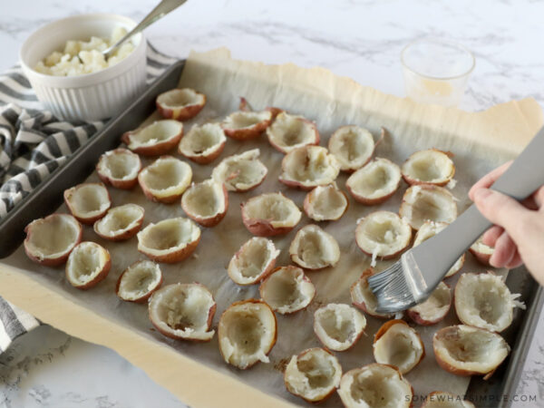 scooping potato filling out of potato skins and brushing with melted butter