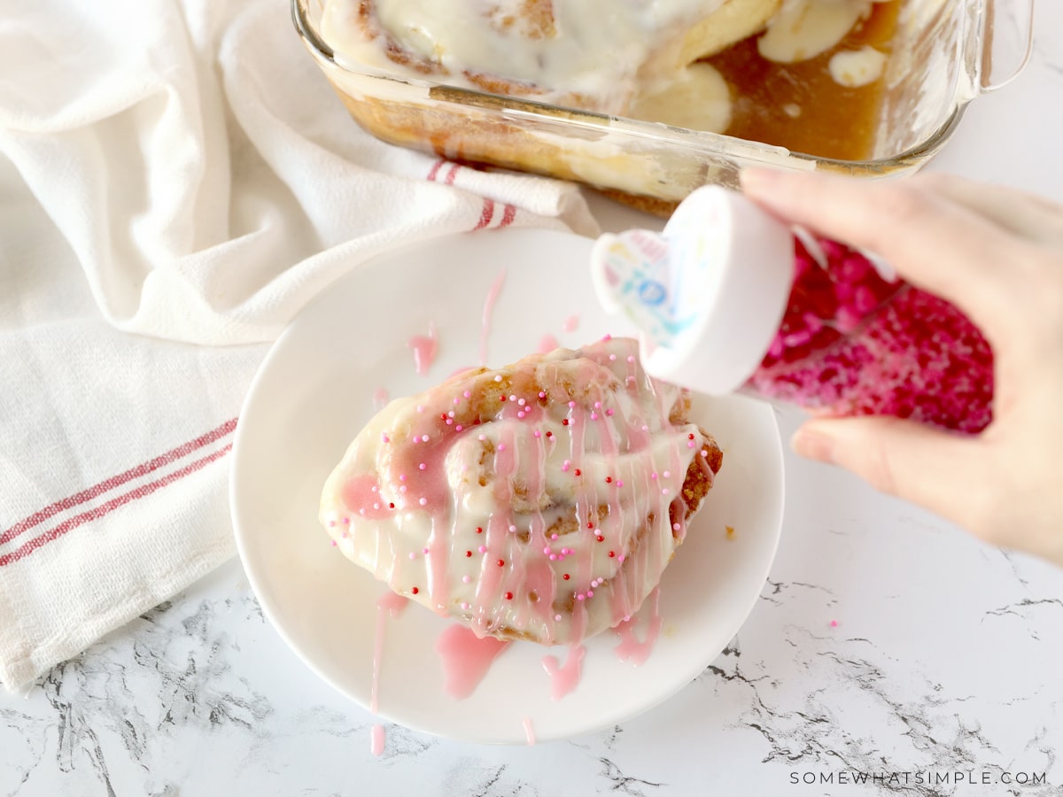 adding sprinkles to the top of valentine cinnamon rolls