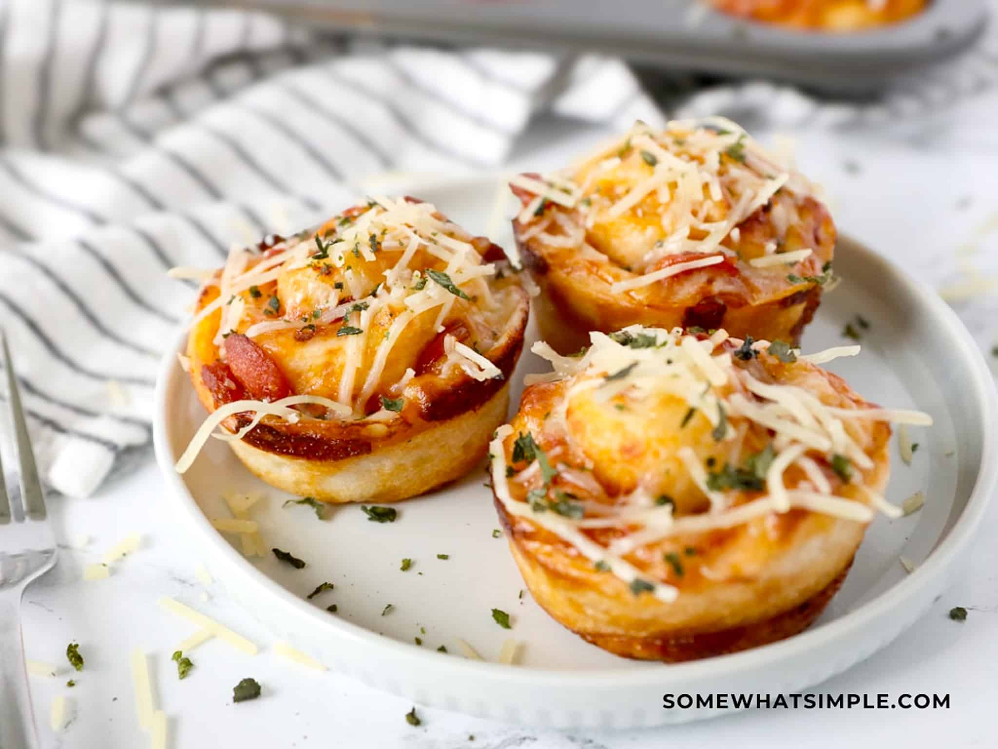 close up of pizza cupcakes on a white plate with parmesan cheese sprinkled over the top
