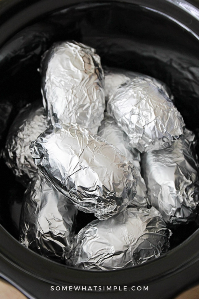 several potatoes wrapped in foil in a crockpot