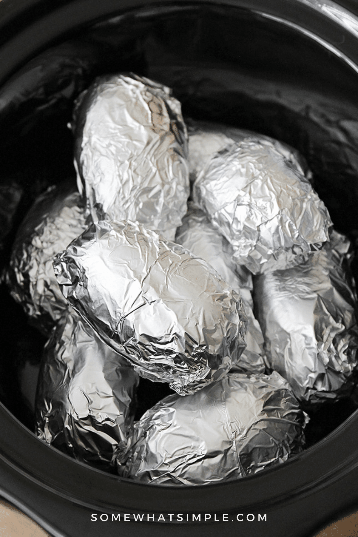 several potatoes wrapped in foil in a crockpot