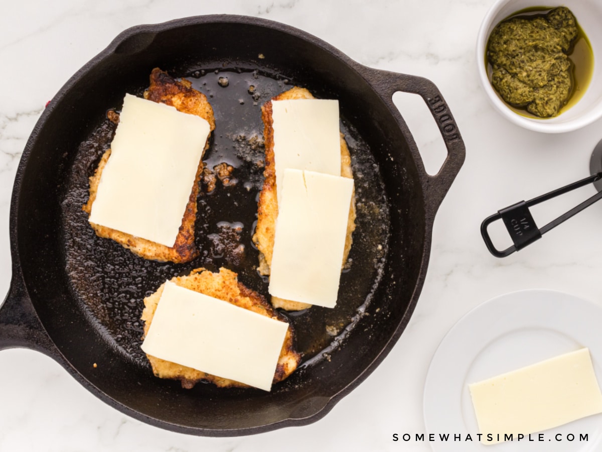 adding slices of cheese on top of breaded chicken breasts in a skillet