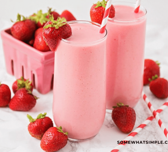 Finished Product of Strawberry Julius in glass cup with strawberries around it