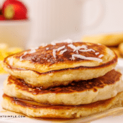 Stack of Coconut Pancakes plated with breakfast foods in the background.
