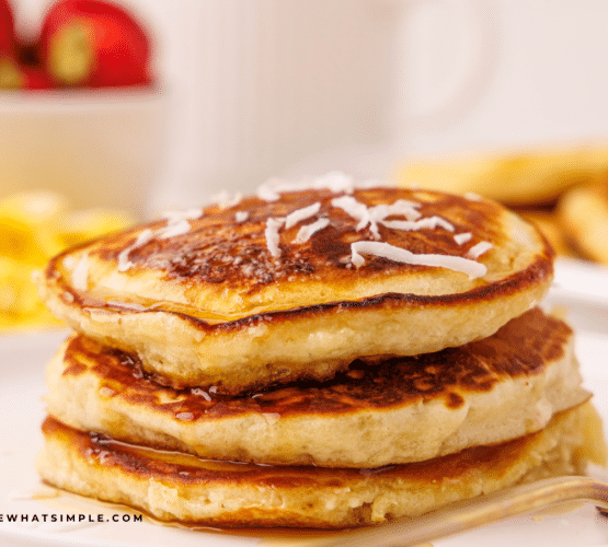 Stack of Coconut Pancakes plated with breakfast foods in the background.