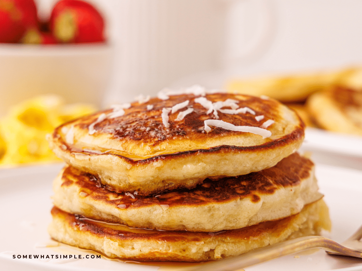 Stack of Coconut Pancakes plated with breakfast foods in the background.