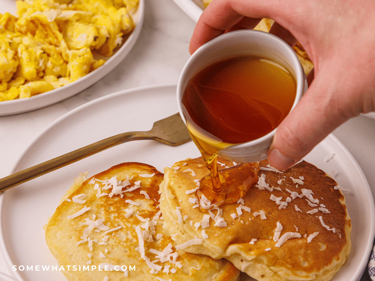pouring syrup over some Coconut Pancakes