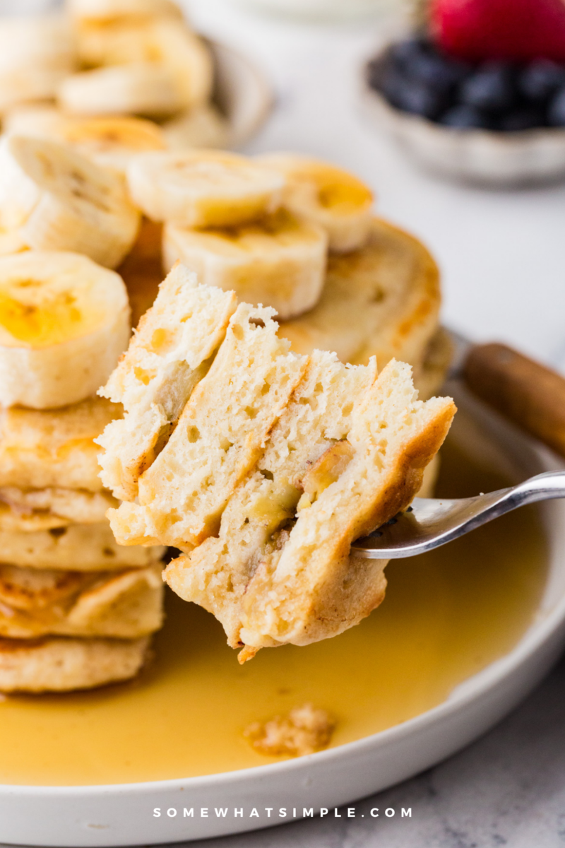 long image of a stack of banana pancakes with a triangle cut out of the stack and onto a fork