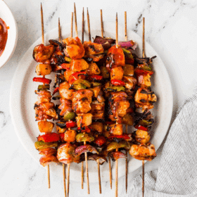 Hawaiian Bacon-Wrapped Chicken Kabobs - plated on a white counter with extra sauce on the side