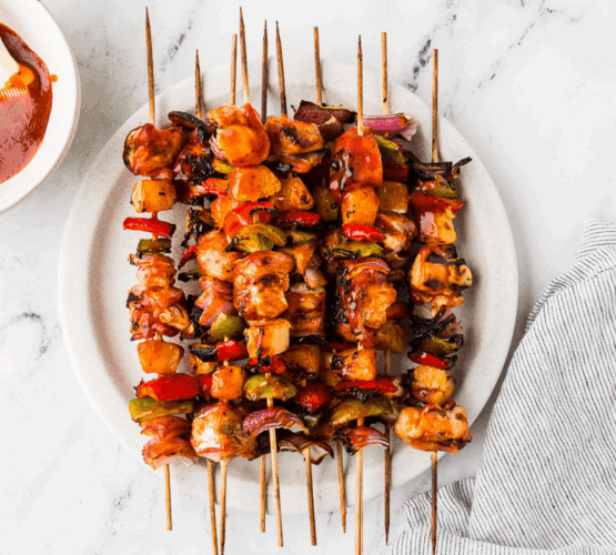 Hawaiian Bacon-Wrapped Chicken Kabobs - plated on a white counter with extra sauce on the side