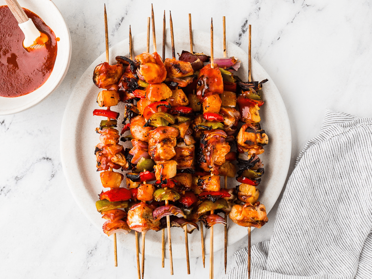 Hawaiian Bacon-Wrapped Chicken Kabobs - plated on a white counter with extra sauce on the side